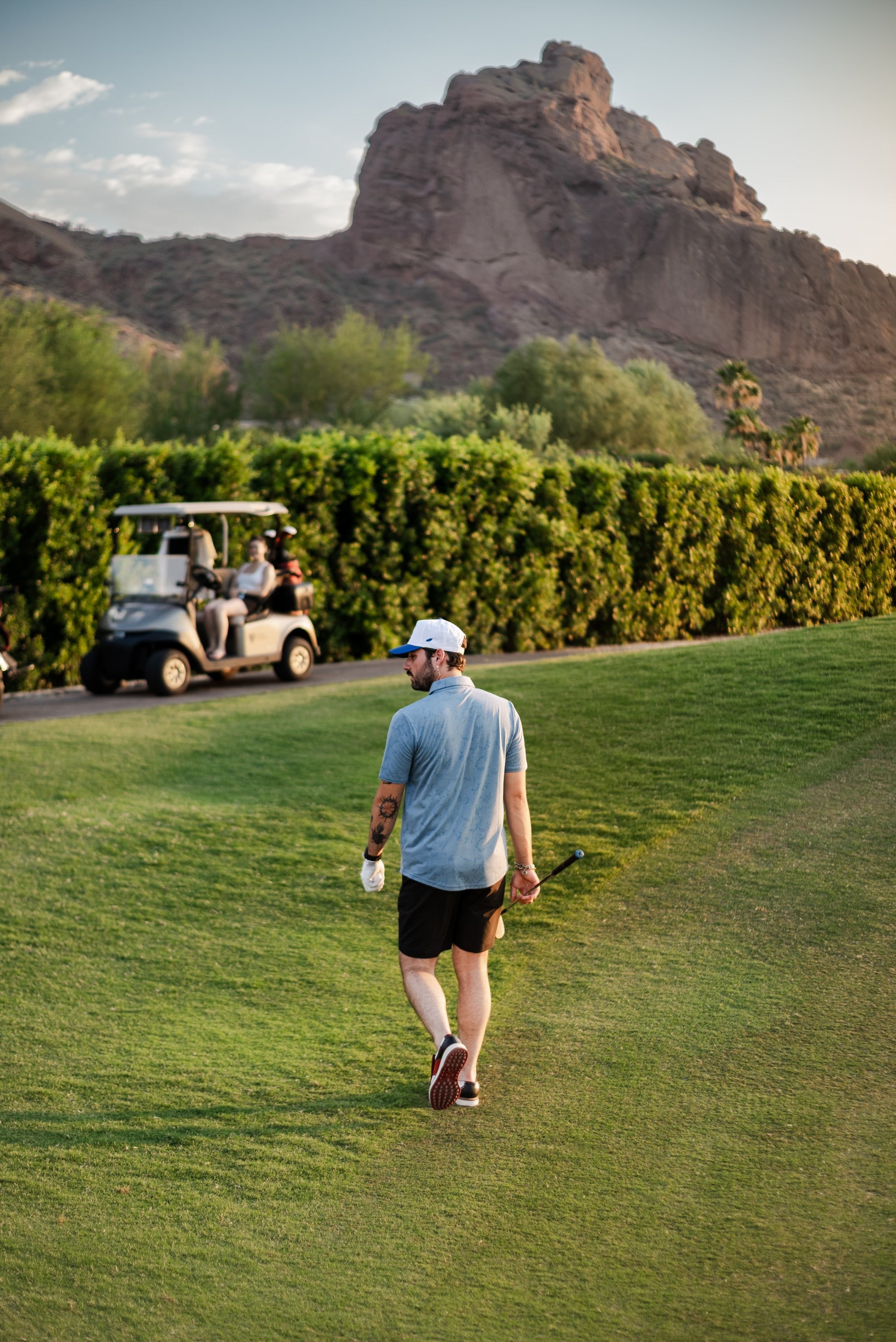 Man with Mallard and Friends White and Royal Blue Five Panel Hat walking towards golf cart